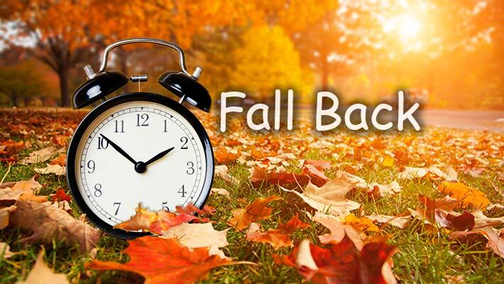 Clock in a field of leaves with the text, Fall Back.