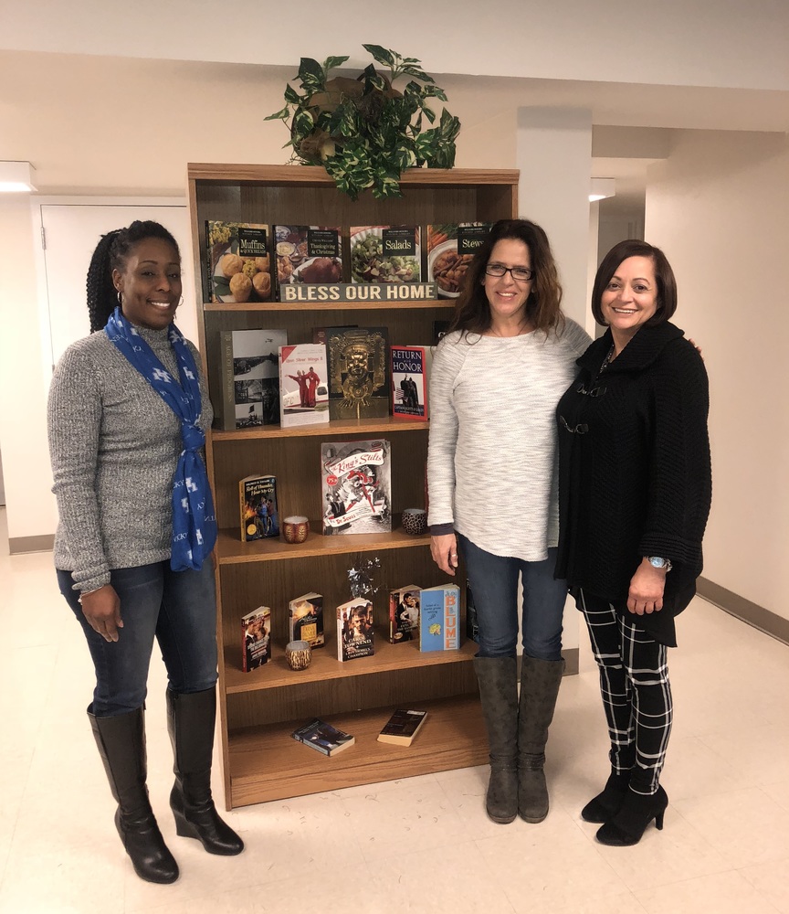 WHHA staff standing next to bookshelf of materials used in Home Library project